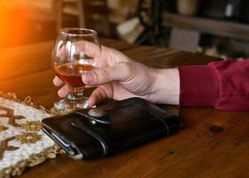 primo piano di un uomo che tiene il suo bicchiere di whisky on the rocks e un sigaro su un elegante tavolo di legno. foto