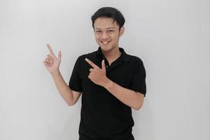 felice e sorriso di giovane uomo asiatico con il punto della mano su uno spazio vuoto. indonesia uomo indossare camicia nera isolato sfondo grigio foto