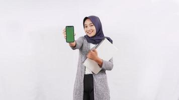 ragazza asiatica che trasporta laptop che mostra lo schermo dello smartphone isolato su sfondo bianco foto