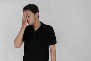 ritratto di giovane uomo asiatico isolato su sfondo grigio che soffre di forte mal di testa, premendo le dita sulle tempie, chiudendo gli occhi per alleviare il dolore con un'espressione facciale indifesa foto