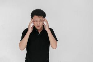 ritratto di giovane uomo asiatico isolato su sfondo grigio che soffre di forte mal di testa, premendo le dita sulle tempie, chiudendo gli occhi per alleviare il dolore con un'espressione facciale indifesa foto
