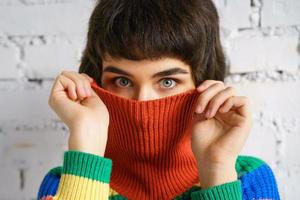 ritratto di una giovane donna con un maglione multicolore, che si copre il viso con un maglione. il concetto di timidezza foto