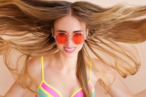 primo piano di ragazza felice in occhiali da sole rosa isolati. vacanze estive e weekend di divertimento. concetto di estate. giovane donna sorridente in costume da bagno di moda. messa a fuoco selettiva. stile di abbigliamento estivo da spiaggia. foto