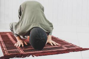 il ritratto del ragazzo musulmano asiatico che indossa il costume tradizionale sta facendo salat con la posa di prostrazione sul tappeto di preghiera foto