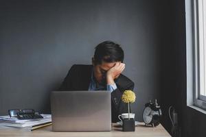 giovane uomo d'affari asiatico stressante e stanco al lavoro. uomo d'affari stanco che si sente stressato, sente affaticamento degli occhi dopo un lungo lavoro d'ufficio su laptop, superlavoro, sindrome dell'ufficio, problemi aziendali. foto