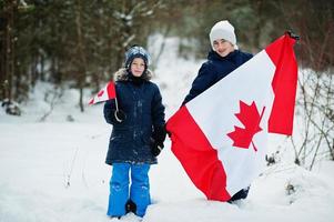 due ragazzi che tengono la bandiera del canada sul paesaggio invernale. foto