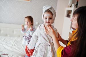 la madre con le figlie in accappatoio con un asciugamano in testa si prende cura della pelle a casa, i cetrioli sugli occhi. foto