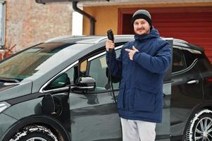 giovane che carica la sua auto elettrica in inverno. concetto di trasporto ecologico. foto