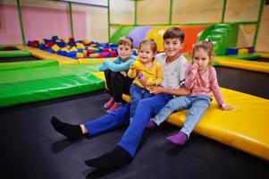 bambini che giocano nel centro giochi al coperto e seduti su un trampolino. famiglia numerosa con quattro figli. foto