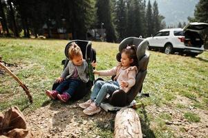 due bambina seduta accanto al falò in montagna. bere acqua dalla bottiglia. clima di escursione autunnale. scaldare e cuocere insieme vicino alla fiamma. foto