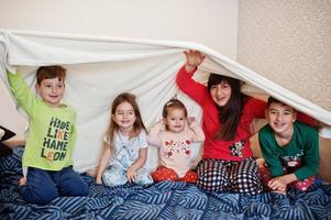 la grande famiglia felice si diverte insieme in camera da letto. concetto di mattina in famiglia numerosa. la madre con quattro bambini indossa il pigiama a letto a casa. foto