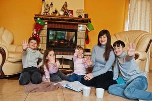 felice giovane famiglia numerosa accanto a un camino nel caldo soggiorno in una giornata invernale. mamma con quattro figli a casa. foto