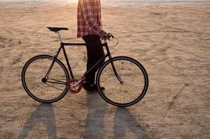 ciclista che cammina con la bici nera retrò durante l'alba nel deserto foto