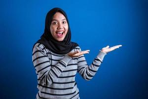 studentessa musulmana asiatica che sorride e indica di presentare qualcosa dalla sua parte foto