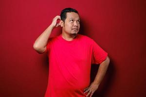 il giovane uomo asiatico indossa una camicia rossa con un gesto di idea di pensiero e sguardo foto