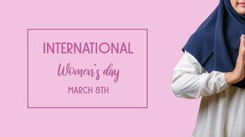 una donna che indossa l'hijab con la mano di saluto di benvenuto su uno sfondo rosa e l'iscrizione giornata internazionale della donna foto