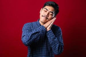 uomo asiatico bello che indossa la camicia che dorme stanco sognando e posando con le mani insieme mentre sorride con gli occhi chiusi foto