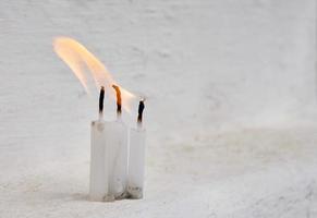 tre candele bianche con fiamma sullo sfondo bianco sporco foto