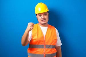 operaio edile asiatico uomo che indossa giubbotto arancione e casco di sicurezza con pugno chiuso foto