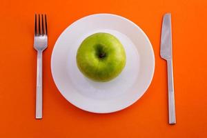 su un piatto una mela verde e un coltello con una forchetta su uno sfondo arancione foto