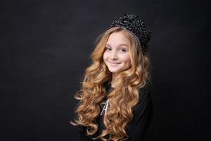 adorabile bambina sorridente felice nella corona della principessa che celebra sul nero foto