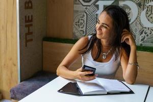 giovane donna seduta al bar al tavolo e digitando un messaggio sullo smartphone. foto