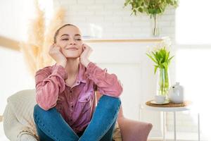 sorridente ragazza caucasica millenaria seduta in appoggio su una sedia in abiti casual foto