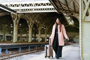 bella giovane donna turistica casual con una valigia in un cappotto rosa in attesa foto