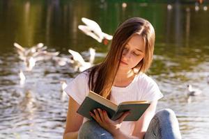 una giovane donna seduta in riva al lago a leggere un libro foto