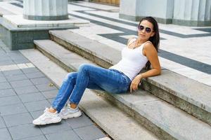 ritratto di attraente donna felice seduta sulle scale in strada di città che indossa foto
