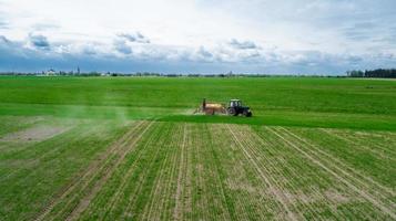 vista aerea, l'agricoltore su un trattore con uno spruzzatore produce fertilizzante per le verdure giovani foto