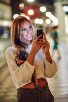 donna che fotografa con lo smartphone di notte in strada foto
