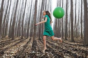 bella ragazza bionda, vestita di verde, che salta nel bosco con un palloncino. foto