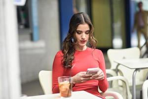 giovane donna che guarda il suo smartphone seduto in un caffè foto