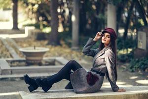 giovane bella ragazza che indossa cappotto invernale e berretto seduto su una panchina nel parco urbano. foto