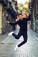 giovane uomo barbuto che salta in strada urbana indossando abiti casual. foto