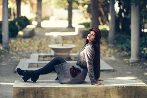 giovane bella ragazza che indossa cappotto invernale e berretto seduto su una panchina nel parco urbano. foto