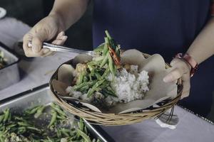 la mano della persona mette le verdure bianche dalla padella d'acciaio al piatto di carta di legno durante il pranzo al ristorante foto