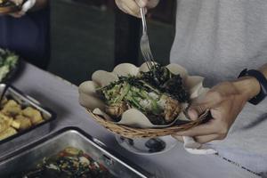 la mano della persona mette le verdure bianche dalla padella d'acciaio al piatto di carta di legno durante il pranzo al ristorante foto