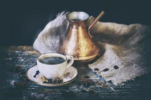 tazza di caffè e caffettiera turca con chicchi di caffè sdraiato su un tavolo di legno squallido foto