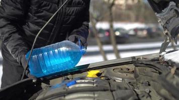 uomo che versa un liquido antigelo in un serbatoio lavavetri di un'auto foto