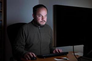 uomo seduto davanti al computer di notte foto
