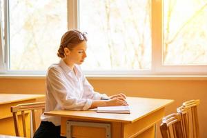 studente carino seduto con un taccuino alla scrivania vicino alla finestra, vista premurosa foto