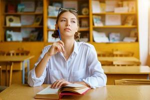 una giovane donna seduta a una scrivania con una camicia bianca, un libro sul tavolo, una bellissima studentessa foto