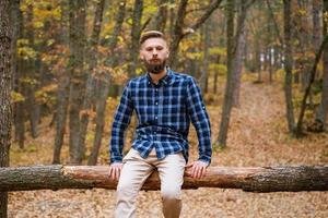 il giovane uomo caucasico con la barba in una camicia a quadri viaggia da solo nella foresta autunnale foto