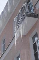 vista dal basso di pericolosi ghiaccioli taglienti appesi al tetto e al balcone. foto