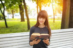 una giovane donna nel parco che legge un libro in una soleggiata giornata estiva foto