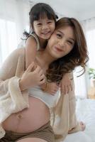 donna incinta seduta sul letto con la giovane figlia foto