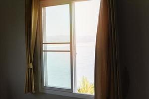 finestra vista mare spiaggia e montagne nel letto in camera da letto mattina e luce solare - vetro della finestra con tendaggi foto