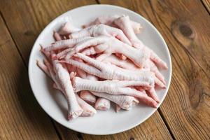 piedi di pollo crudi freschi per cibi cotti sullo sfondo della cucina del tavolo in legno, piedi di pollo sul piatto bianco foto